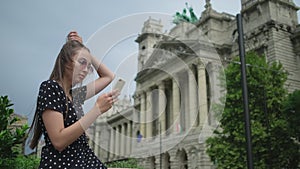 Young woman using smartphone, Budapest Ethnographic Museum in background