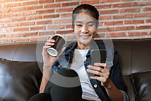 Young woman using smartphone and holding coffee cup at cafe