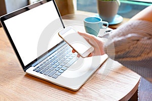 A young woman using smartphone and laptop in cafe.