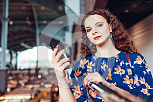 Young woman using smartphone and looking at camera after shopping in mall