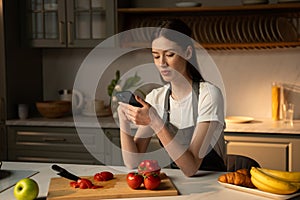 Young Woman Using Smartphone in Modern Kitchen While Preparing Fresh Vegetables