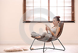 Young woman using smartphone near window with blinds at home