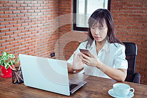 young woman is using smartphone and notebook computer in office