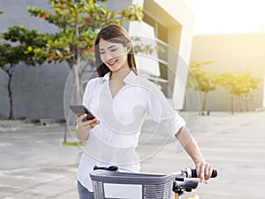 Young woman using smartphone while riding bike on sunny day.Bike sharing service.Health lifestyle