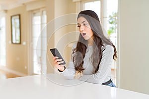 Young woman using smartphone sending a message scared in shock with a surprise face, afraid and excited with fear expression