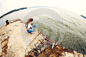 Young woman using smartphone sitting on an old pier