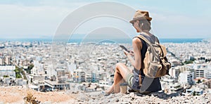 Young woman using smartphone during vacations. Girl holding mobile phone with a big city at background. Travel, lifestyle, tourist