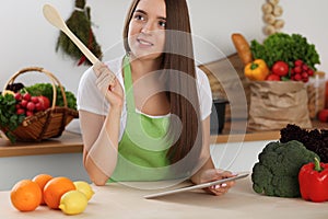 Young woman using tablet computer while cooking in kitchen. Householding, tasty food and digital technology in lifestyle