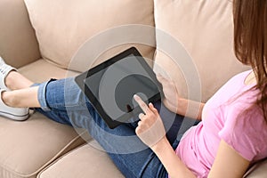 Young woman using tablet computer for online food delivery while resting on sofa indoors