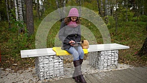 Young woman using tablet computer while sitting on bench in autumn park. Student with a Tablet Sitting on the Bench and