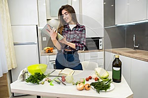 Young woman using a tablet computer to cook different vegetables in her kitchen for everything about healthy nutrition