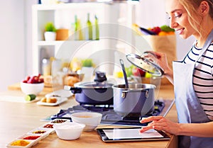 Young woman using a tablet computer to cook in her kitchen