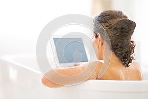 Young woman using tablet pc in bathtub. rear view