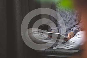 Young woman using tablet pc relaxing in cozy house, sitting on chair. Front view, selective focus photo