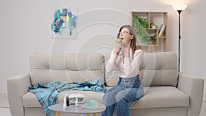 Young woman using throat spray sitting on the sofa at home