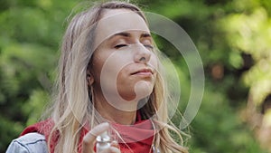 Young woman using throat spray standing on the park background. Health and medical concept.