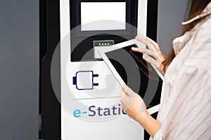 Young woman using touchscreen tablet, connecting to electric car charge station