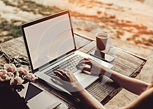 Young woman using and typing laptop computer at rough wooden table with coffee cup, strawberries