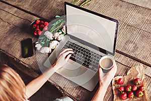 Young woman using and typing laptop computer at rough wooden table with coffee cup