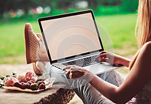 Young woman using and typing laptop computer at rough wooden table with coffee cup, strawberries