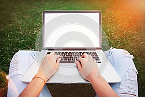 Young woman using and typing laptop computer in summer grass. Fr