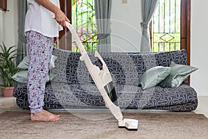 Young woman using a vacuum cleaner while cleaning carpet in the house