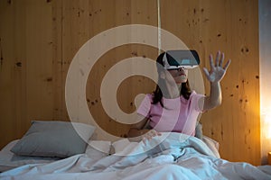 Young woman using virtual reality headset in bed. VR, Future digital technology, game, movies entertainment, metaverse, NFT and 3D