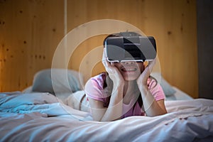 Young woman using virtual reality headset in bed. VR, Future digital technology, game, movies entertainment, metaverse, NFT and 3D