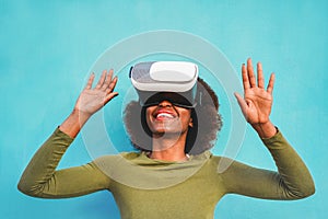 Young woman using virtual reality headset with blue wall in background - African woman having fun with new trend technology - Tech