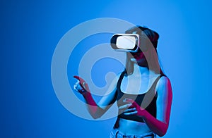 Young woman using virtual reality headset in neon light. VR, future, gadgets, metaverse, technology, education online