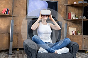Young woman using virtual reality headset while sitting in gray armchair