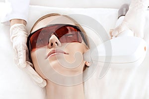 Young woman in uv protective glasses receiving laser skin care on face