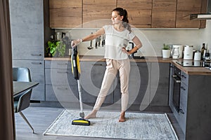 Young woman after vacuuming carpet with wireless vacuum cleaner in kitchen. Household and useful technology concept.