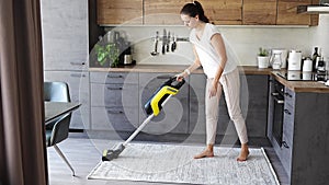 Young woman vacuuming carpet with wireless vacuum cleaner in kitchen. Household and useful technology concept.