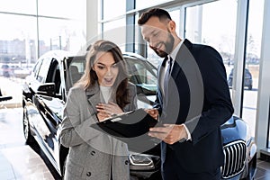 young woman versed in auto insurance pole together with consultant in car dealership photo