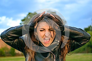 Young woman very angry, shouting and stressed with hands on hair at the park