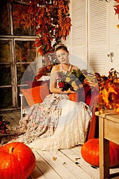 Young woman in vintage dress on autumn porch. Beauty girl in fa
