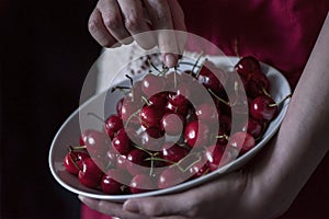 A young woman with a vintage kitchen apron holding a cherry bowl on a black background, close up