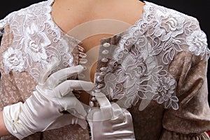 A young woman in vintage lingerie and white gloves unzips her girlfriend`s dress, a lot of buttons. Added a small grain, imitatio