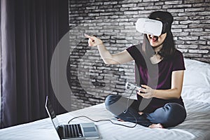 Young woman in virtual reality headset or 3d glasses playing video game and pointing in the air, gaming and technology concept