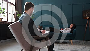 Young woman visiting male psychologist lying on the comfortable couch during psychological session in the luxury blue