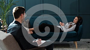 Young woman visiting male psychologist lying on the comfortable couch during psychological session in the luxury blue