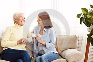 Young woman visiting senior mother and drinking coffee together