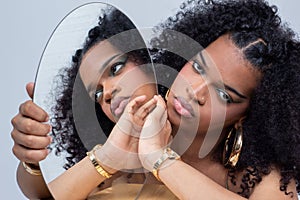 Young woman with voluminous Afro hairstyles posing with a mirror