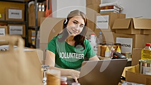 Young woman volunteer using laptop and headphones smiling at charity center