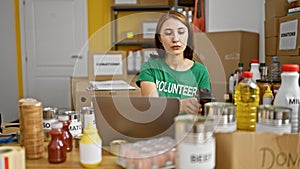 Young woman volunteer using laptop scanning products at charity center