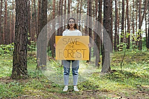 Young woman volunteer in the woods pickets and holds a poster save the forest