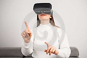 Young woman in VR glasses moves hand sitting on couch