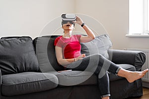 Young woman with VR set sitting on the couch in living room at home. VIrtual reality travel, shopping, learning