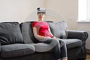 Young woman with VR set sitting on the couch in living room at home. VIrtual reality travel, shopping, learning